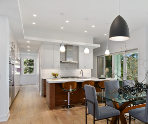 Kitchen Lighting Requests: Modern kitchen with white cabinets, a wooden island, and hanging pendant lights. The adjacent dining area features a glass table, grey chairs, and a large black pendant light. Light wood flooring throughout.